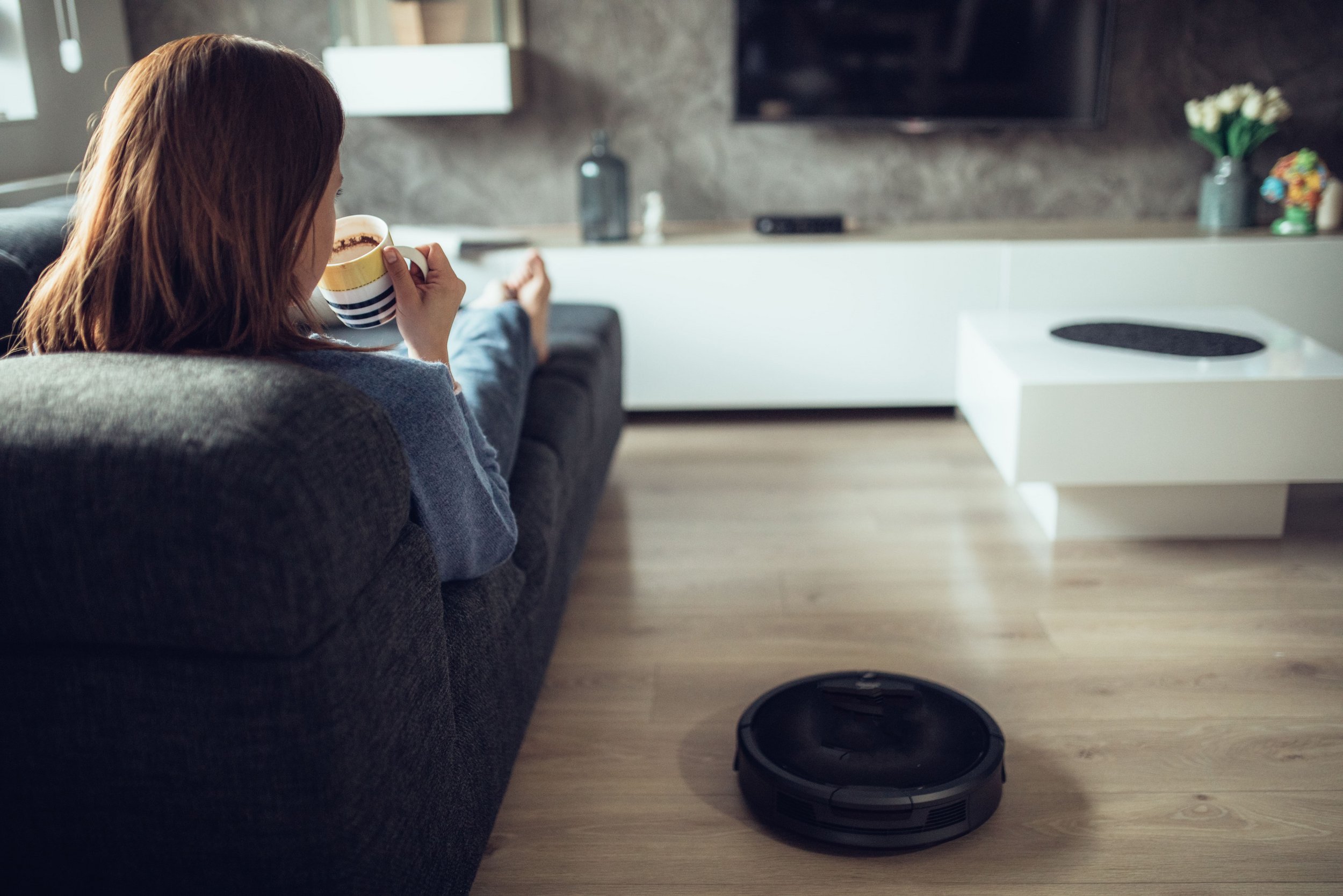 Woman relaxing on sofa next to vacuum cleaner robot